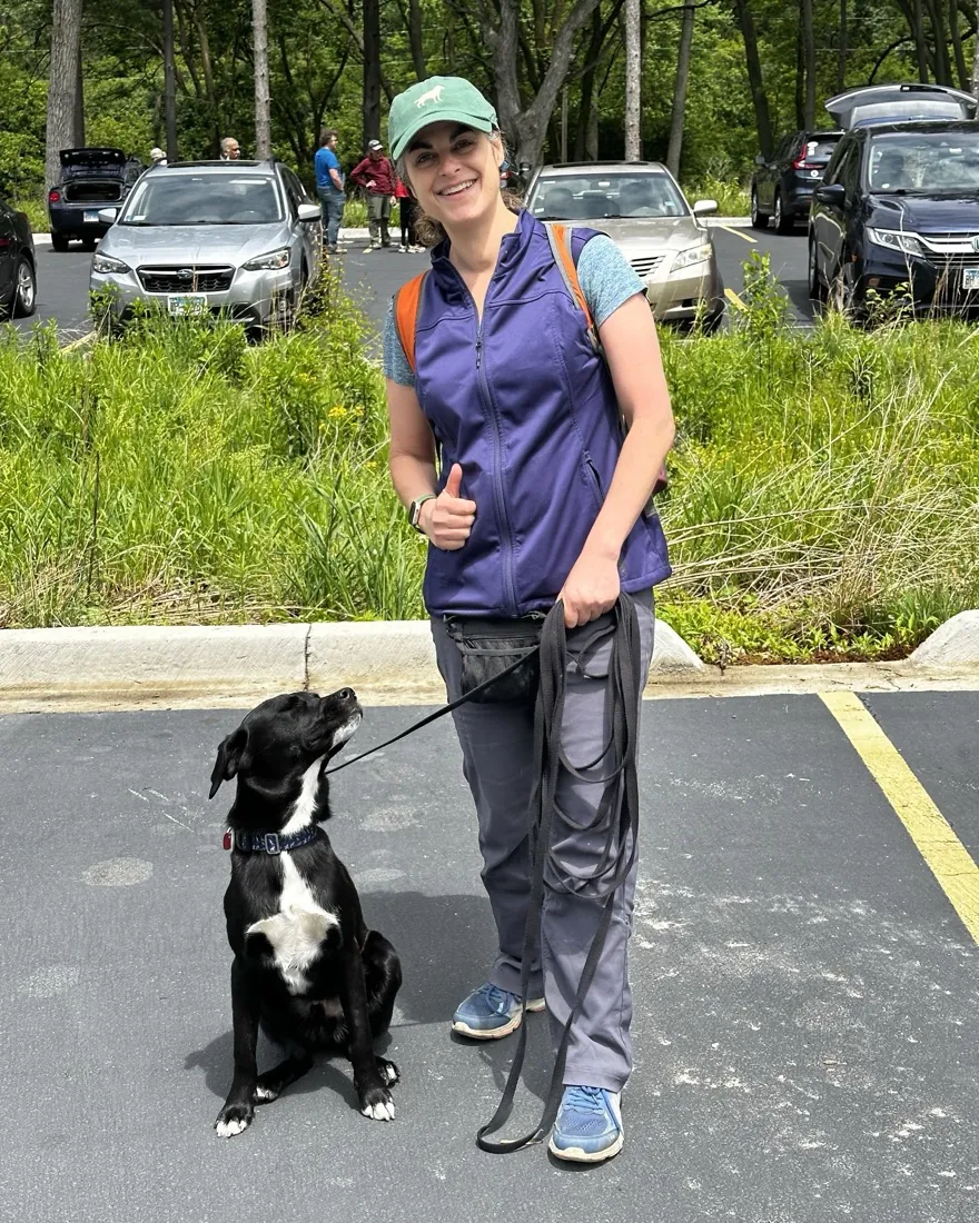 Alicia smiling in a parking lot with a black-and-white dog at her side